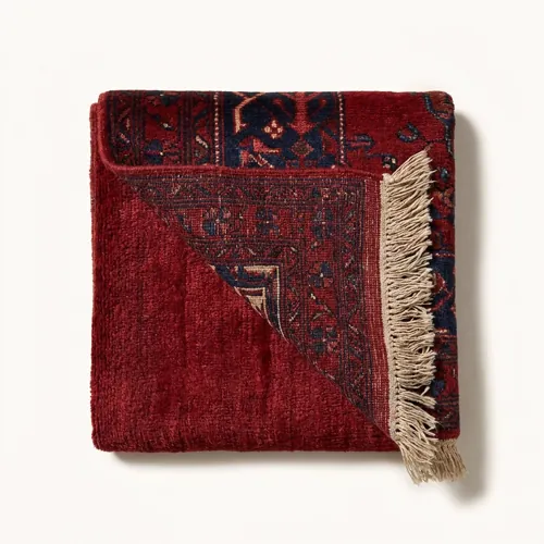 A deep red Hamadan carpet folded back to show the pile and the fringe